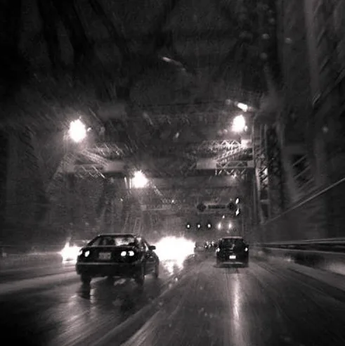 A black-and-white photo of cars driving through a snowy tunnel with blurred motion and bright headlights. The overlaid text…
