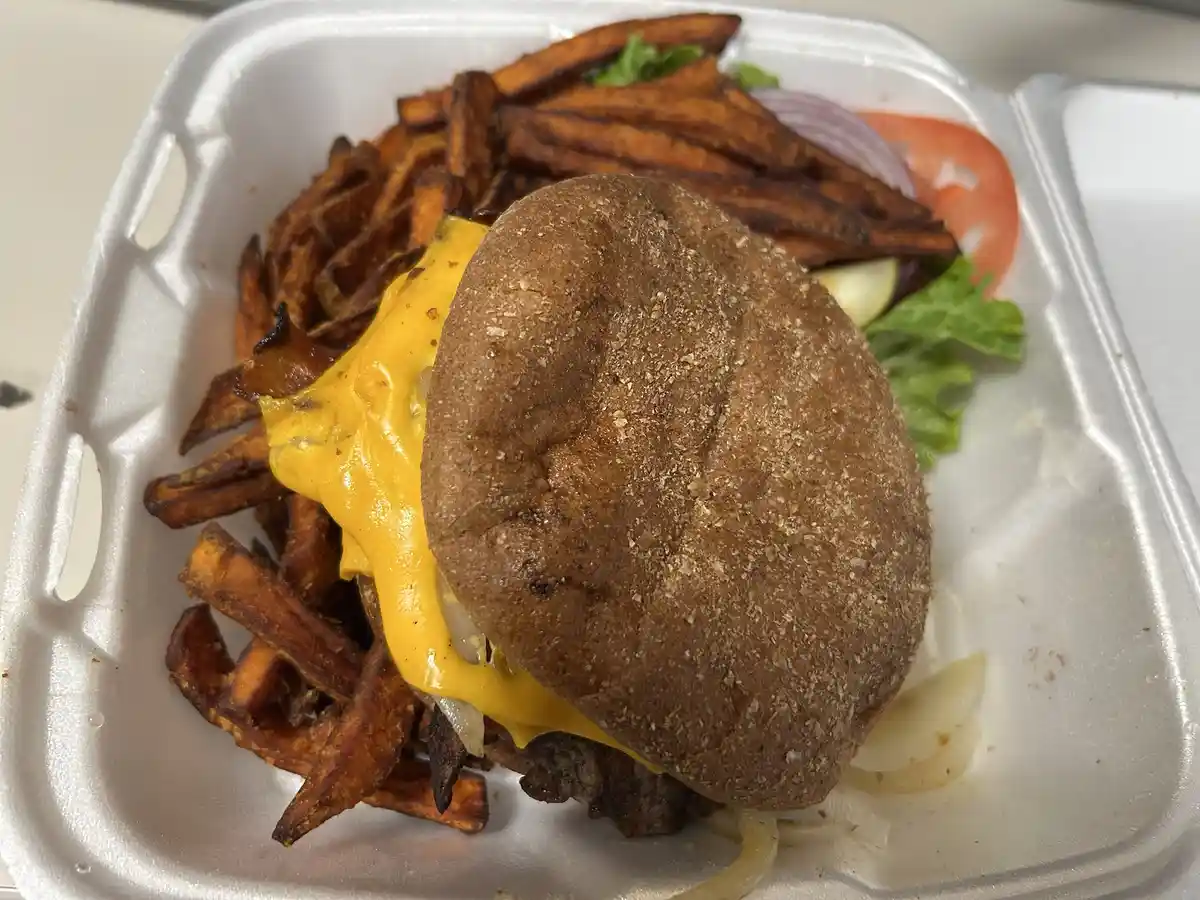 A close-up photo of a cheeseburger with a whole wheat bun, melted yellow cheese, and visible meat patty, served in a white…