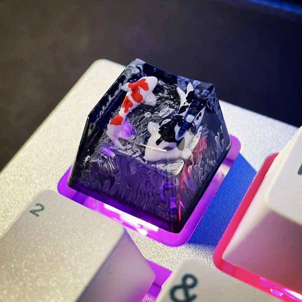 A close-up photo of a custom mechanical keyboard keycap with a translucent purple base, embedded with detailed resin artwork…