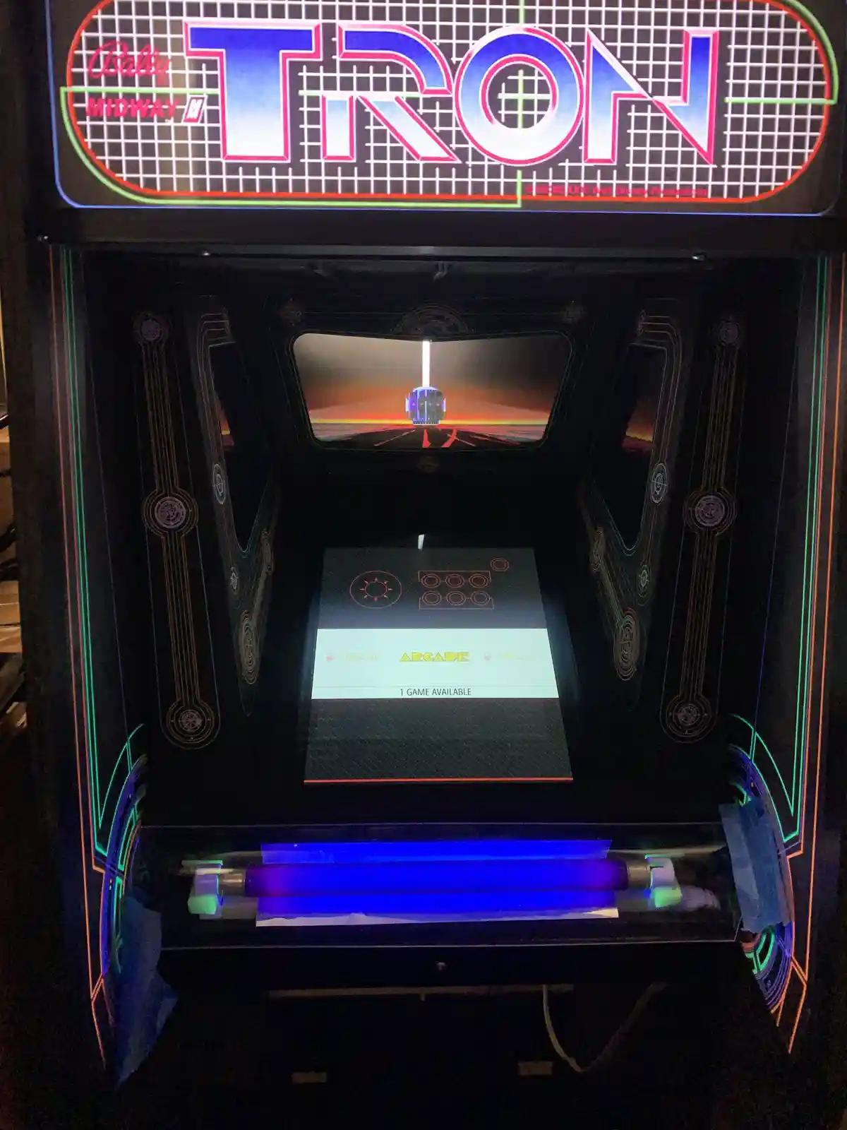 A vintage Bally Midway 'TRON' arcade machine, featuring its iconic grid-patterned marquee and glowing neon lights, displays…
