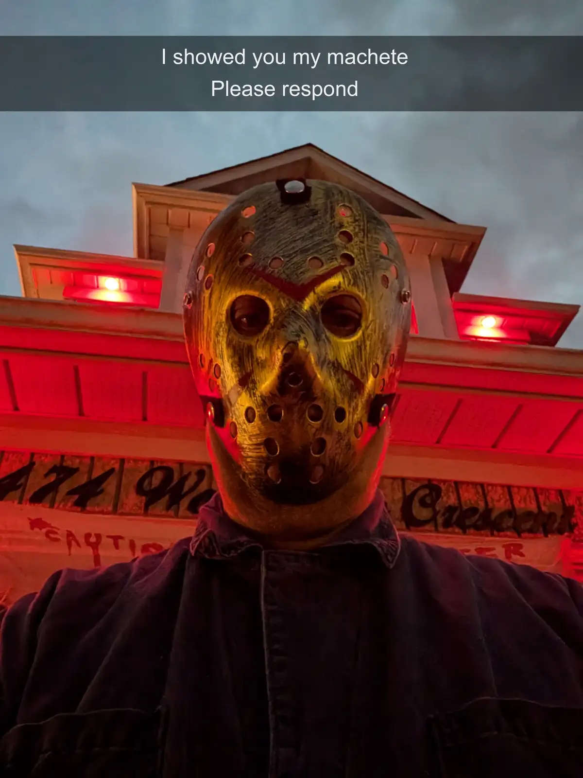 A person wearing a Jason Voorhees hockey mask from the 'Friday the 13th' franchise stands in front of a building with red…