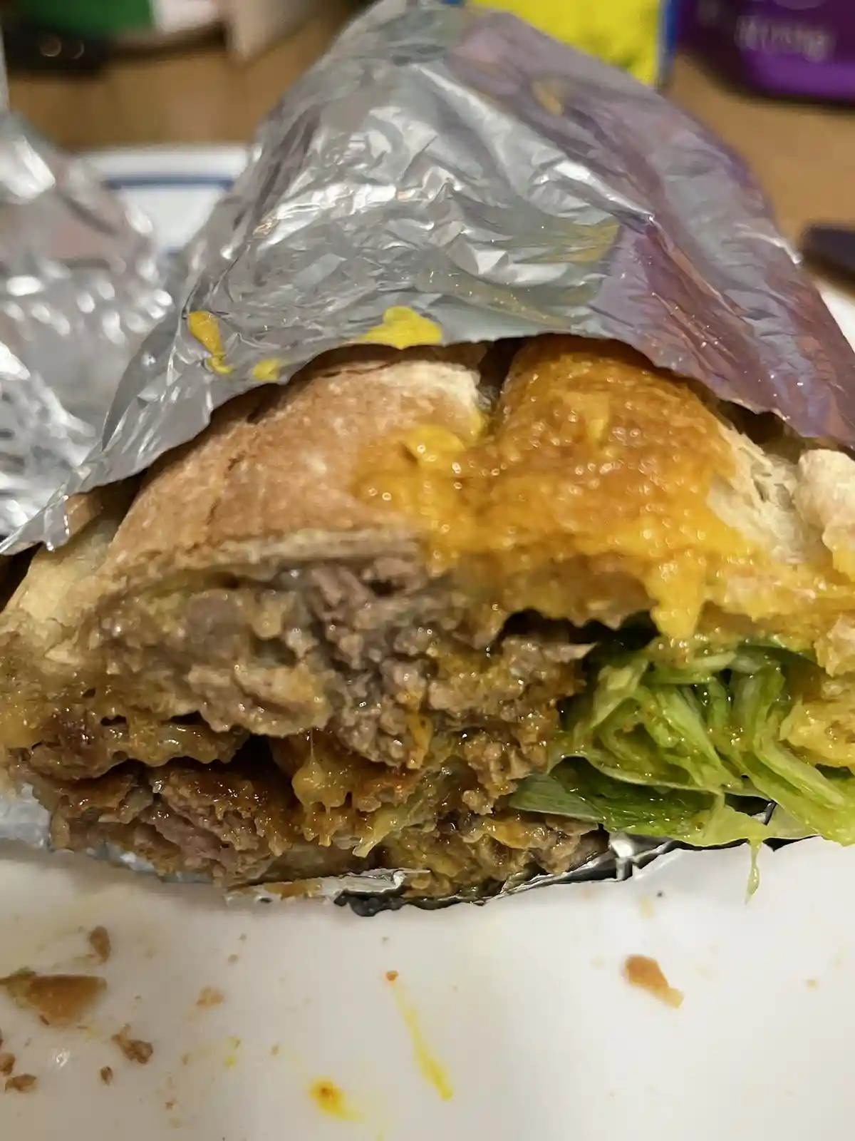 A close-up photo shows a partially unwrapped burger in foil, revealing melted cheese, ground beef, and lettuce inside a bun…