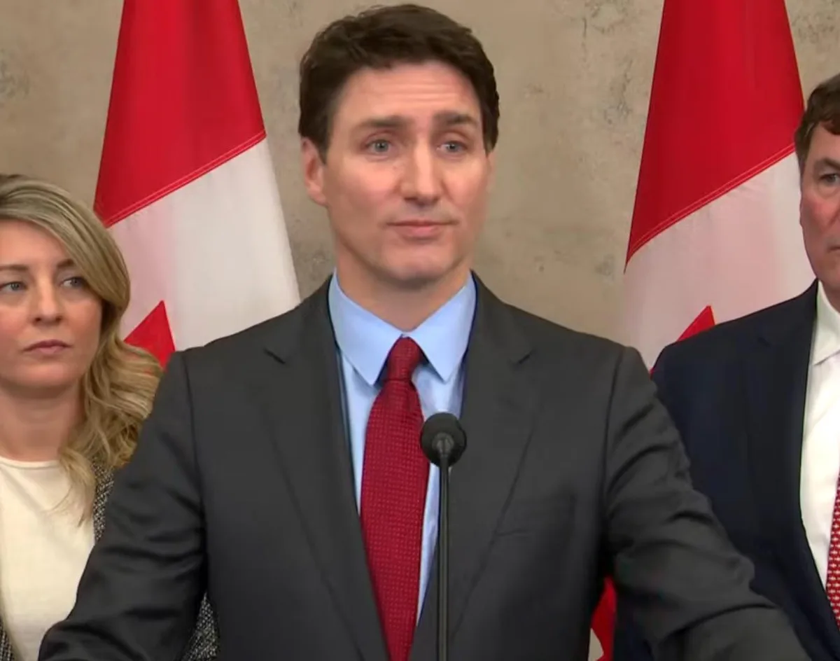 a still image of canadian prime minister justin trudeau standing at a podium with two canadian flags behind him, wearing a…