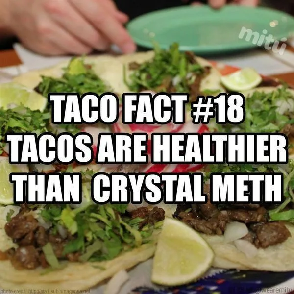 A close-up photo of several tacos topped with meat, cilantro, and lime wedges, with a hand and green plate visible in the…