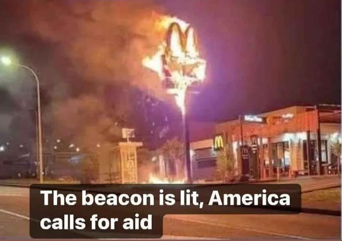 A nighttime photo shows a McDonald's restaurant with its iconic golden arches sign engulfed in flames and smoke, while the…