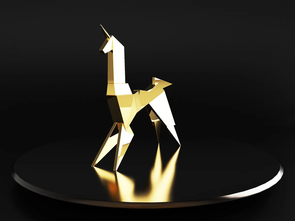 A stylized, geometric golden unicorn statue with sharp facets and a single horn stands on a black circular pedestal against…