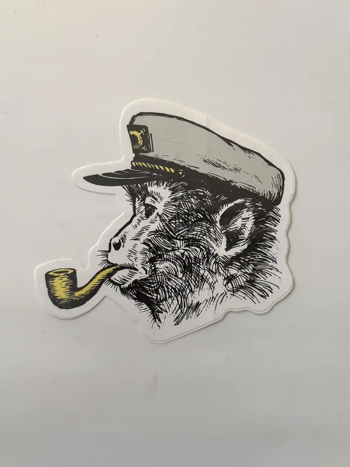 A sticker depicts a monkey in profile wearing a captain's hat with an anchor emblem and smoking a yellow pipe. The…
