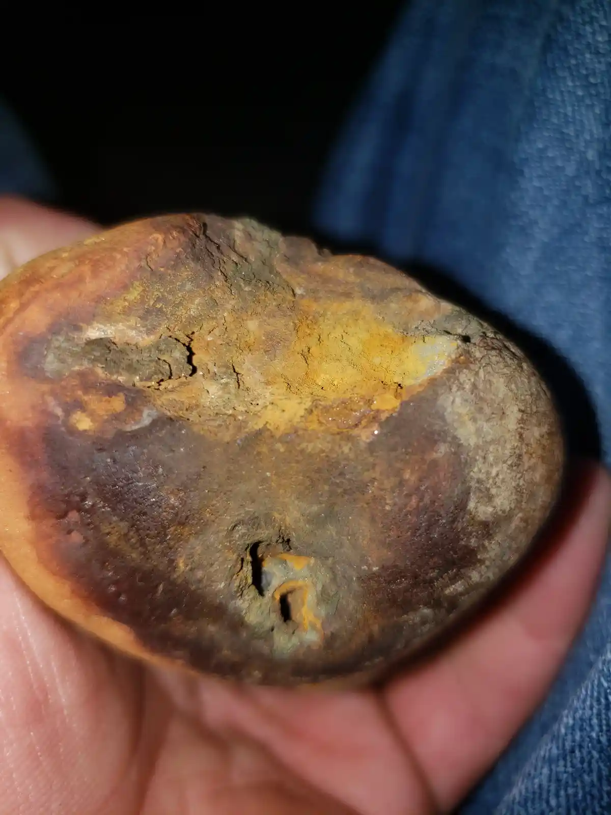 A close-up photo shows a hand holding a weathered, round, brownish rock with visible cracks and discoloration. The rock has…