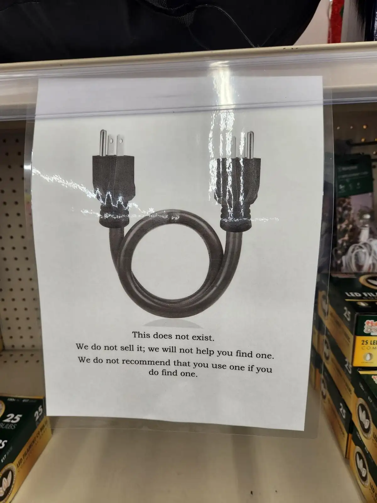 A printed sign in a store aisle shows a drawing of a black electrical cord with two plugs on each end, connected in a loop…