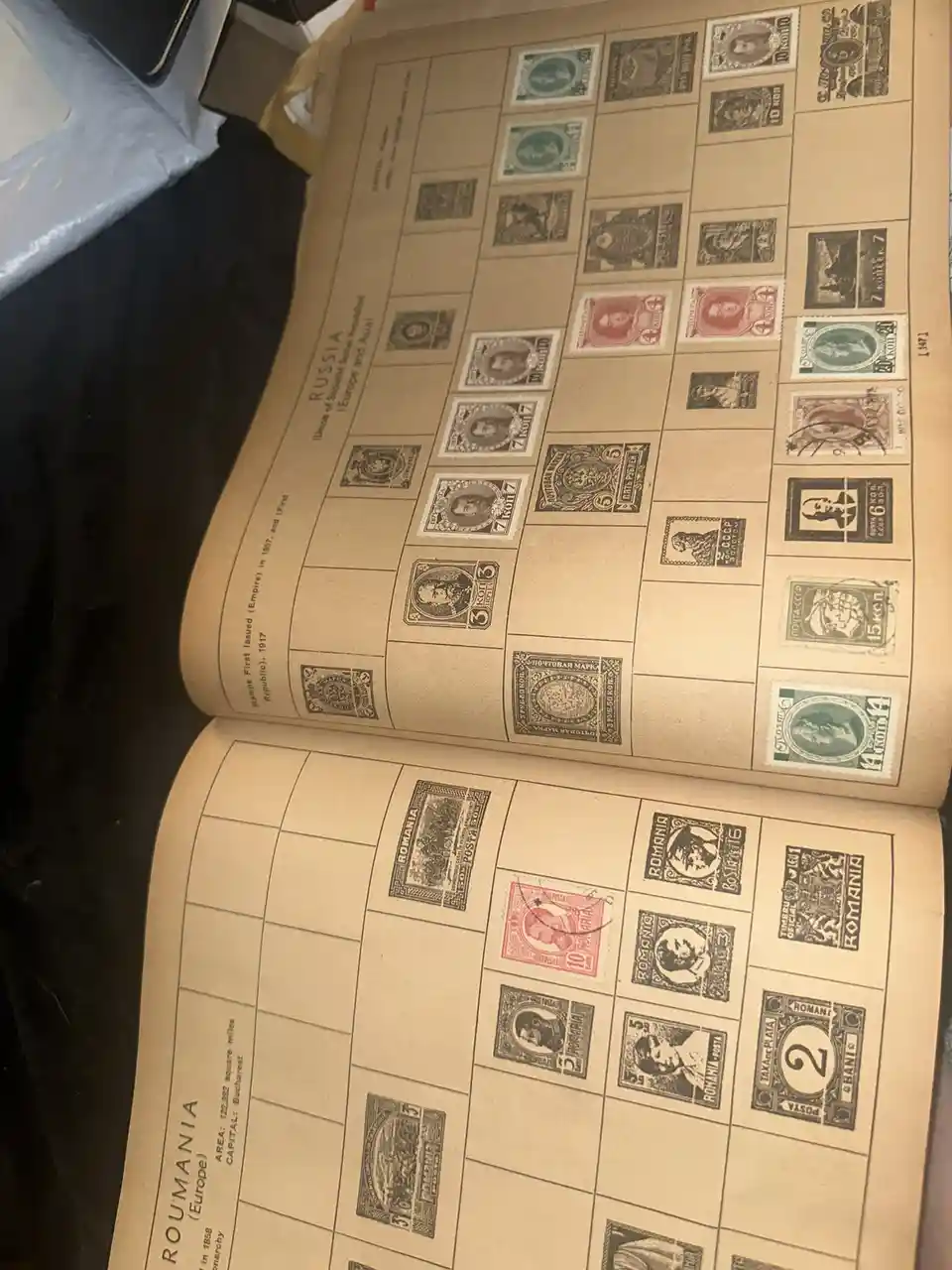 An open stamp album displays meticulously arranged vintage postage stamps in two pages: the top page is labeled 'RUSSIA'…
