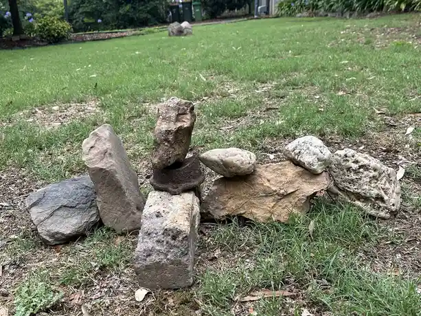 A photo of several rocks arranged in precarious stacks on a grassy lawn, with one stack featuring a rusty metal ring as a…