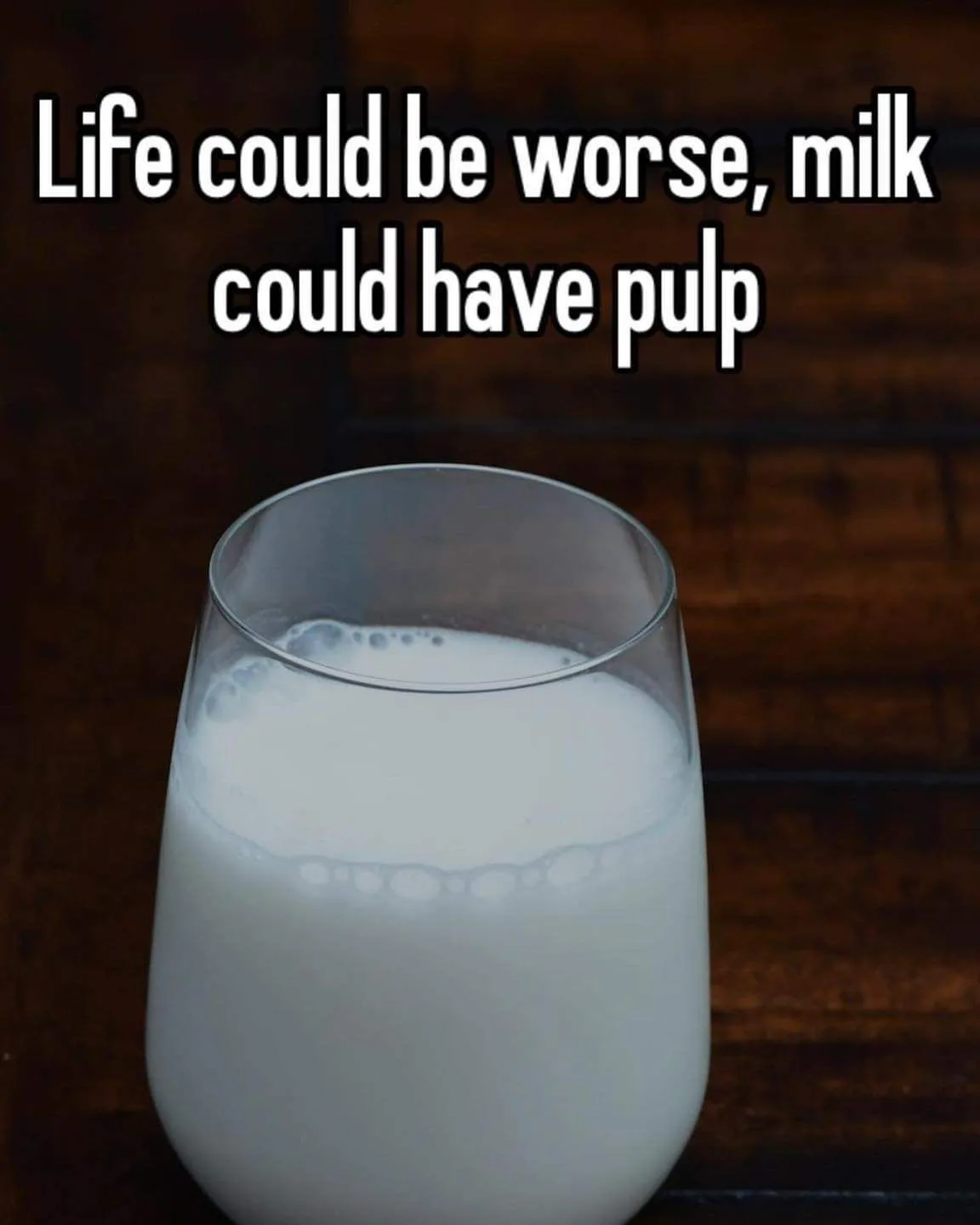 A glass of plain milk sits on a dark wooden surface, with white text overlaid at the top reading 'Life could be worse, milk…