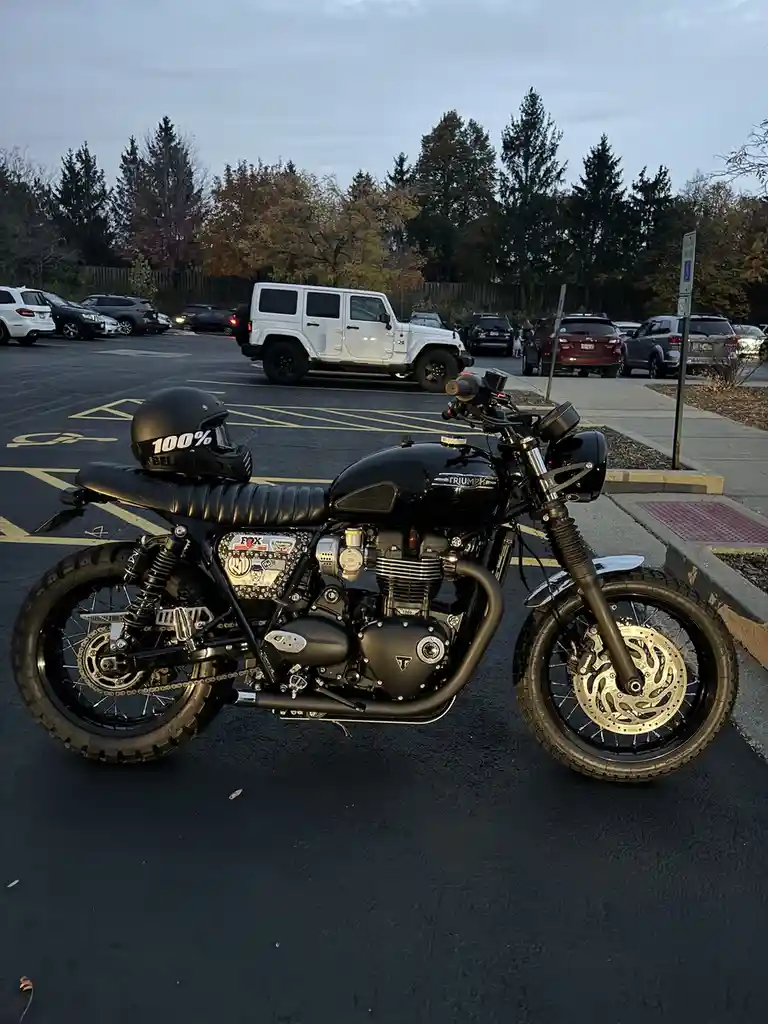 A black Triumph motorcycle is parked in a handicapped parking space in a lot, with a black helmet resting on its seat. The…