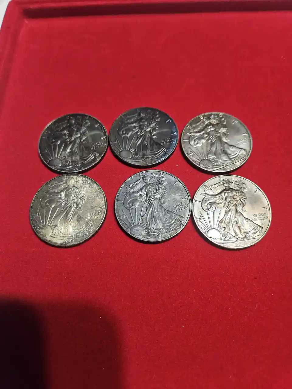 Six identical 2018 American Silver Eagle coins are arranged in two rows on a red velvet surface. Each coin features the…