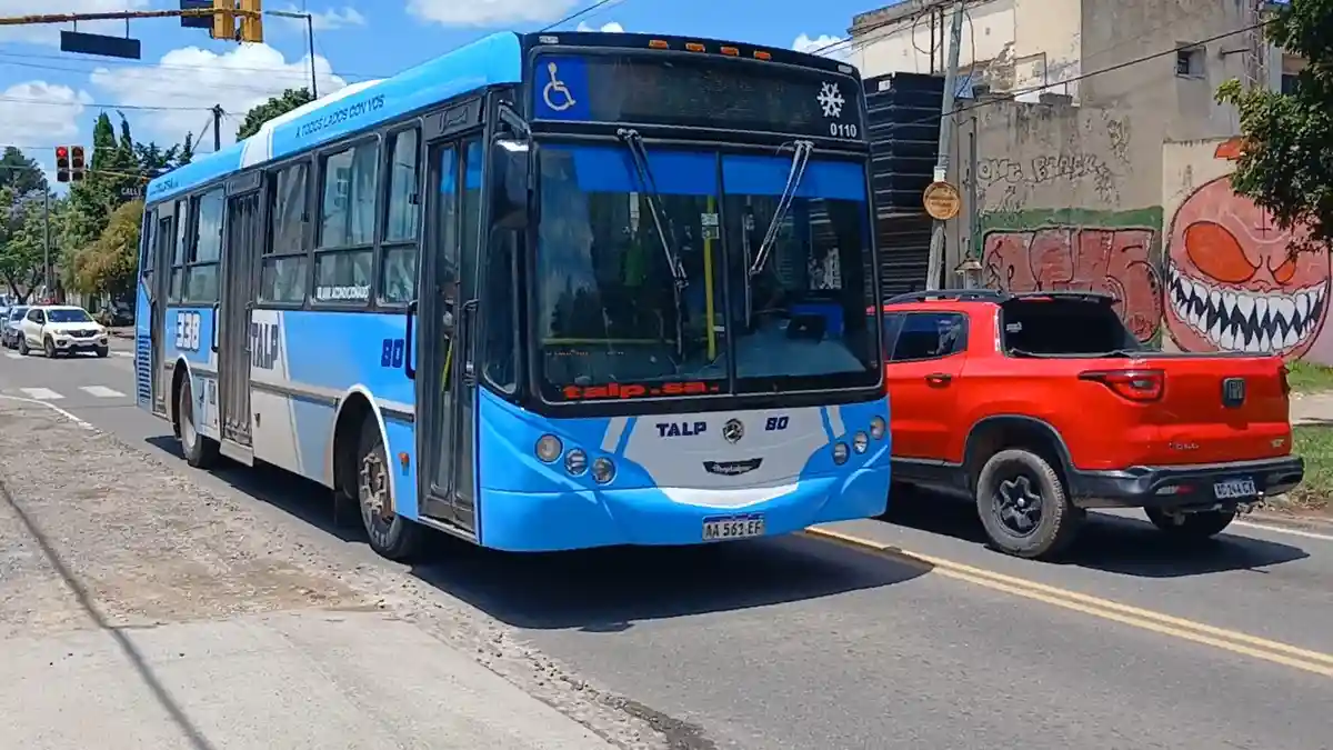 A blue and white public bus labeled 'TALP 80' is stopped at an intersection next to a red SUV. The bus has 'A TODOS LADOS…