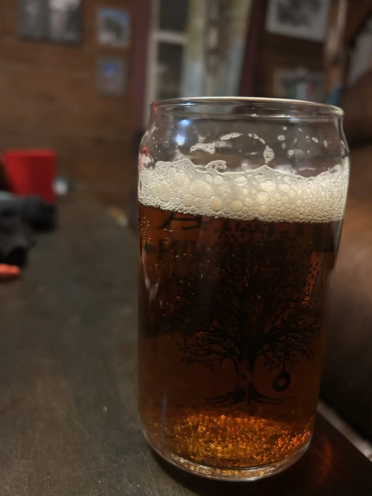 A close-up photo shows a glass mug filled with amber-colored beer, topped with a white foamy head. The glass features a…