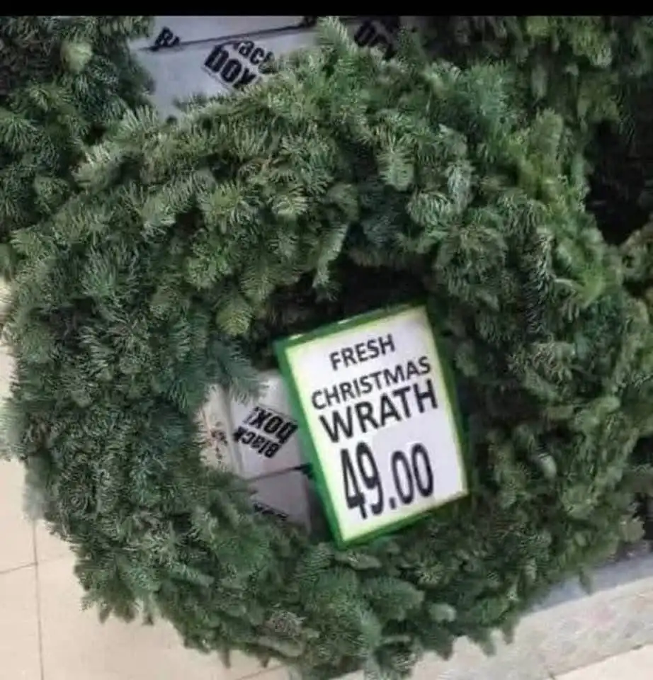 A close-up photo of a green, pine-needle Christmas wreath with a price tag inserted into it. The tag reads 'FRESH CHRISTMAS…