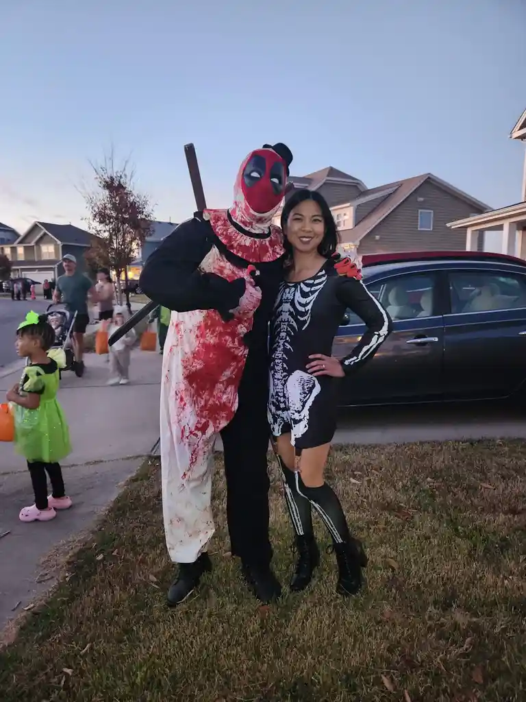 Two people pose for a photo at a Halloween event; one is dressed as Deadpool in a blood-splattered costume holding a weapon…