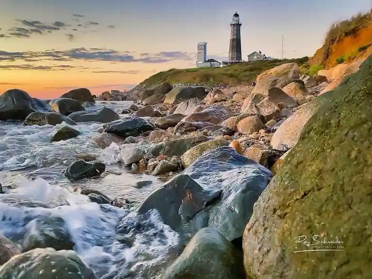 A scenic photograph of a rocky coastline at sunset, featuring crashing waves, large boulders in the foreground, and a…