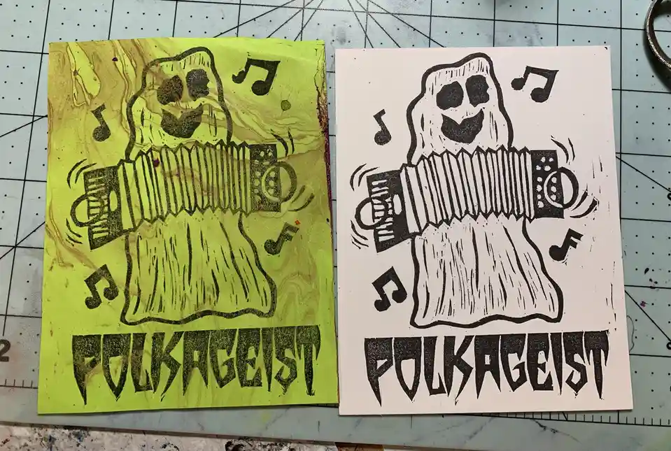 Two hand-drawn prints side-by-side show a smiling ghost playing an accordion with musical notes floating around it. The left…