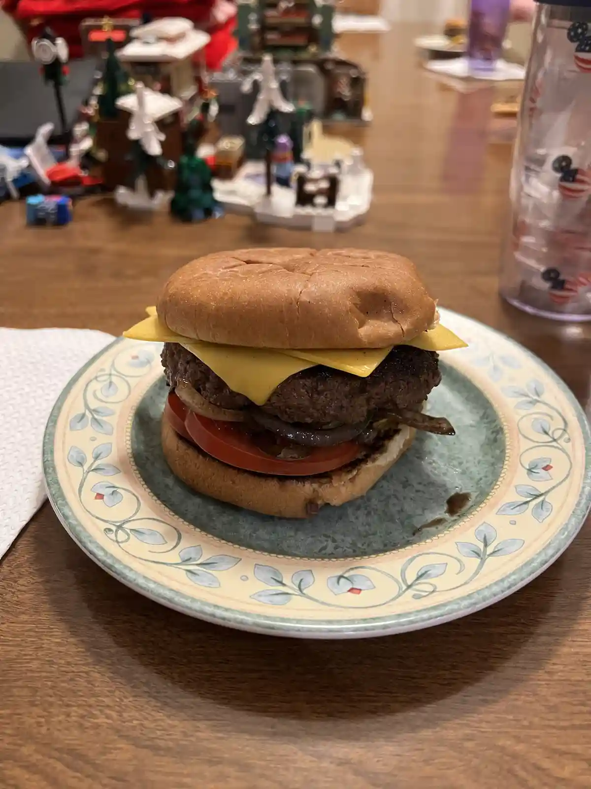 A close-up photo of a cheeseburger on a patterned plate, featuring a beef patty, melted cheese, tomato, and onion between…