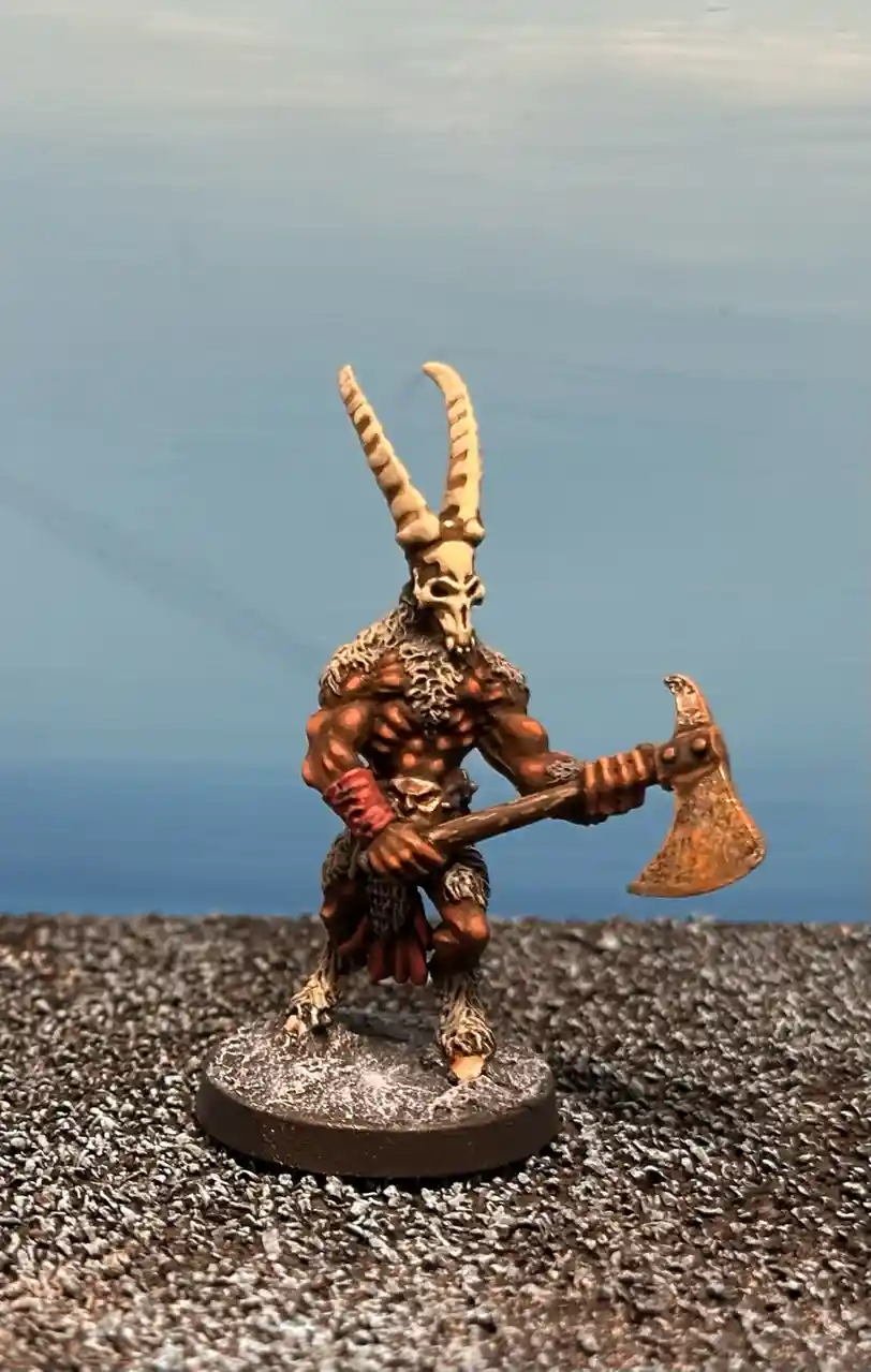 A painted miniature figurine of a muscular humanoid with a skull for a head and large curved horns, wielding a battle axe…