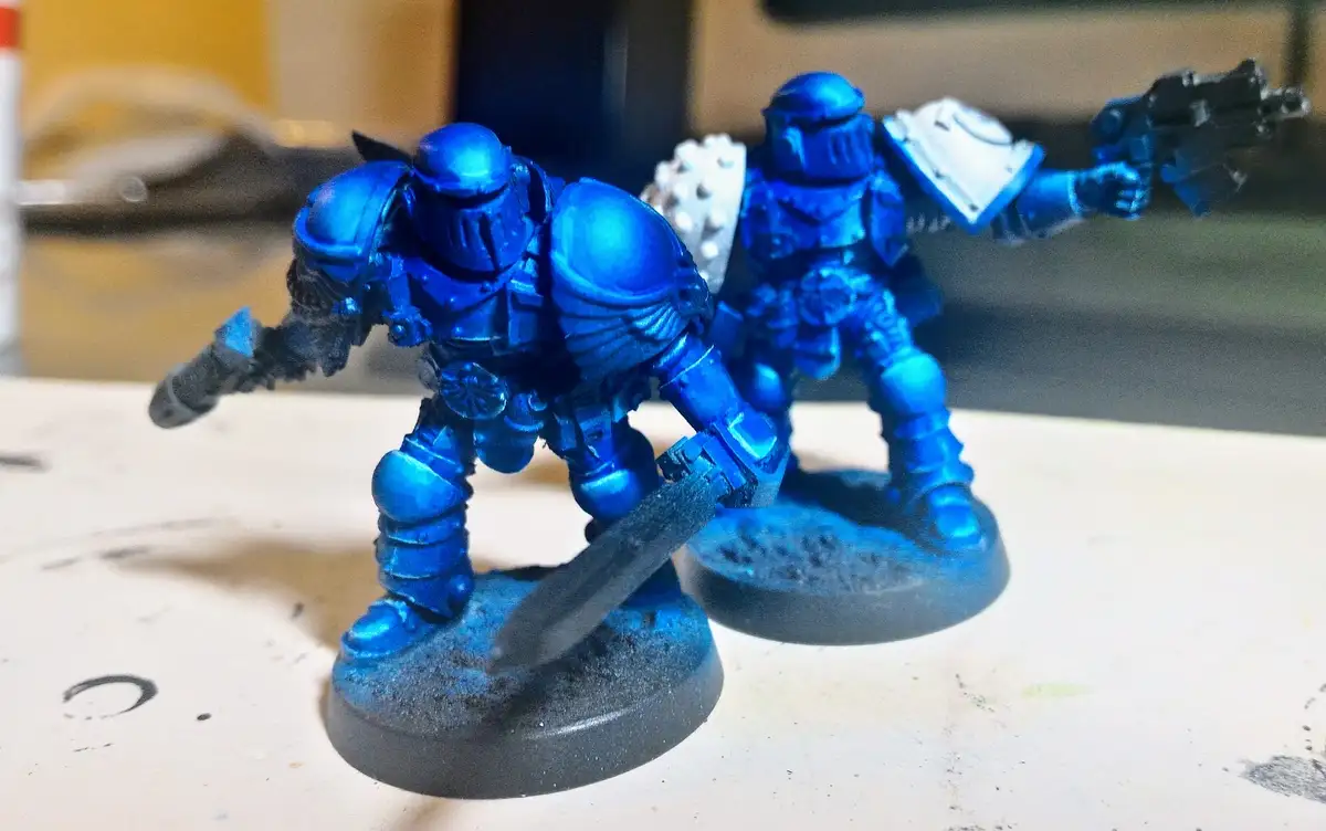 Two heavily armored miniature figurines, likely from a tabletop wargame, are painted a vibrant, uniform blue with black…