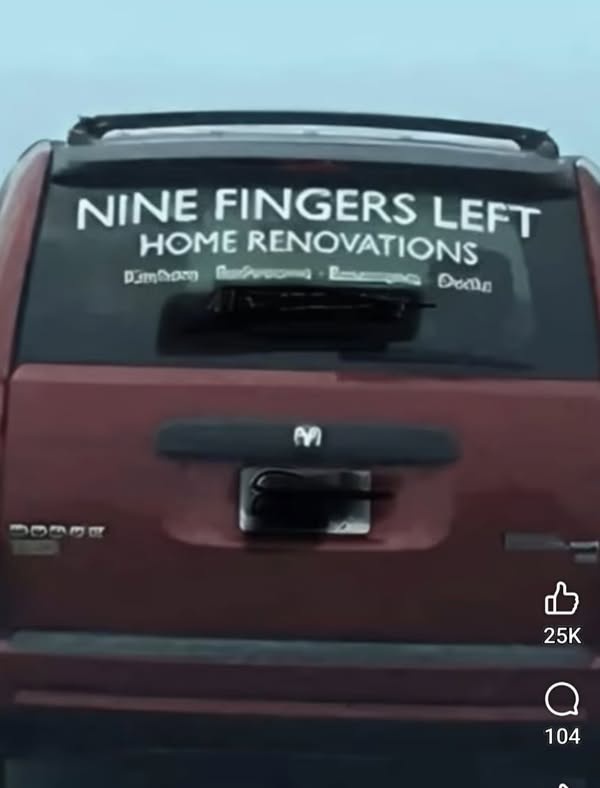 The rear window of a red Dodge SUV displays a white decal that reads 'NINE FINGERS LEFT HOME RENOVATIONS' with smaller…