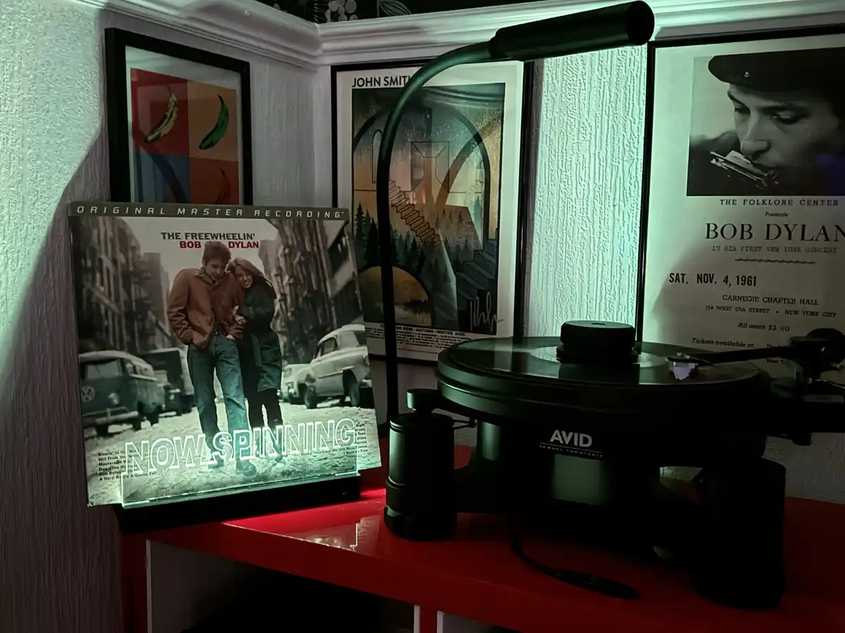 A vinyl record player sits on a red shelf next to a glowing album cover of Bob Dylan's 'The Freewheelin' Bob Dylan'. The…