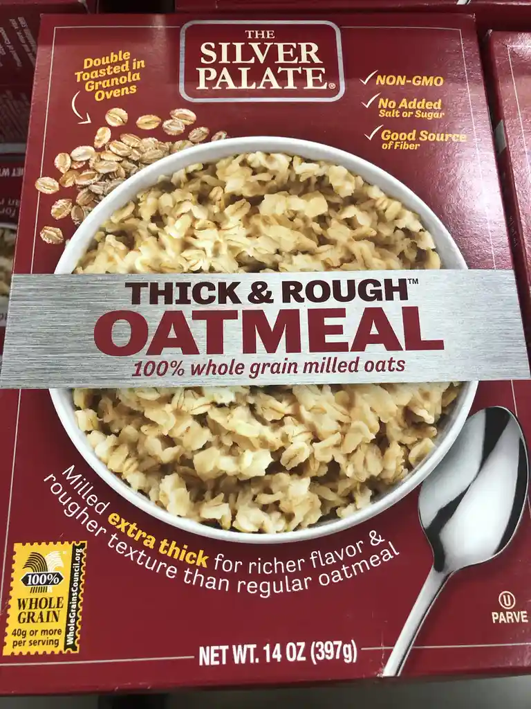 A close-up of a red box of 'The Silver Palate' brand oatmeal, featuring a bowl of thick, rough-textured oatmeal with a spoon…
