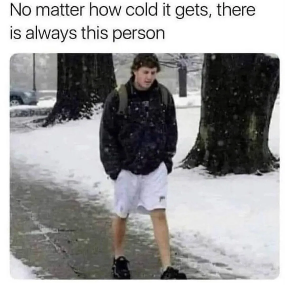 A young man stands outdoors in a snowy environment, wearing a dark jacket and white shorts with black shoes, while snow…