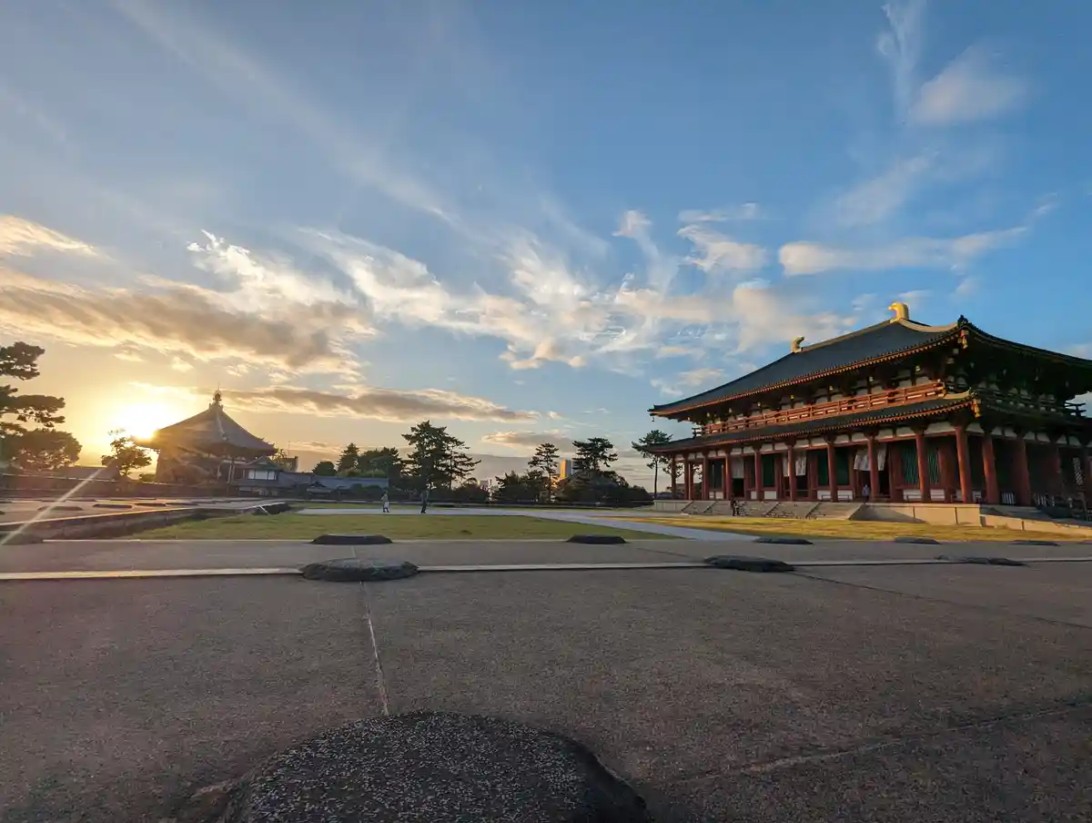 A serene, wide-angle photograph captures a traditional Japanese temple complex at sunset, with a large wooden hall on the…