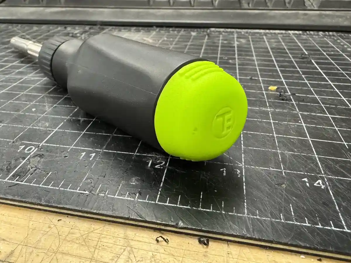 A black and neon green tool with a textured grip lies diagonally on a black cutting mat with white grid lines and numbers…