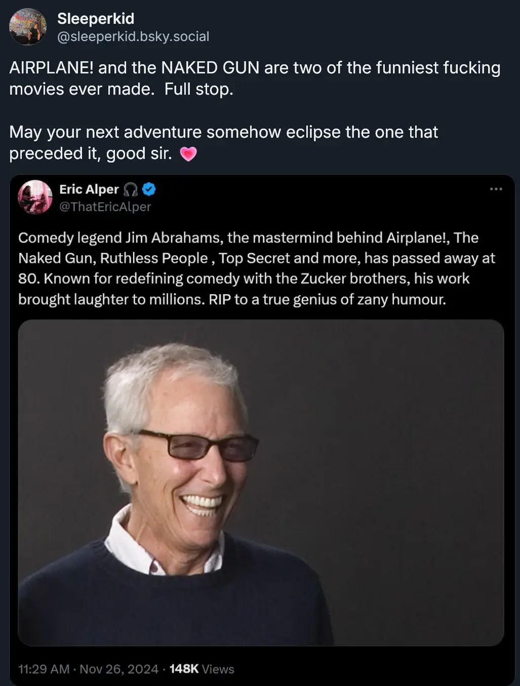 A screenshot of a social media post showing a smiling older man with white hair and glasses, wearing a dark sweater over a…