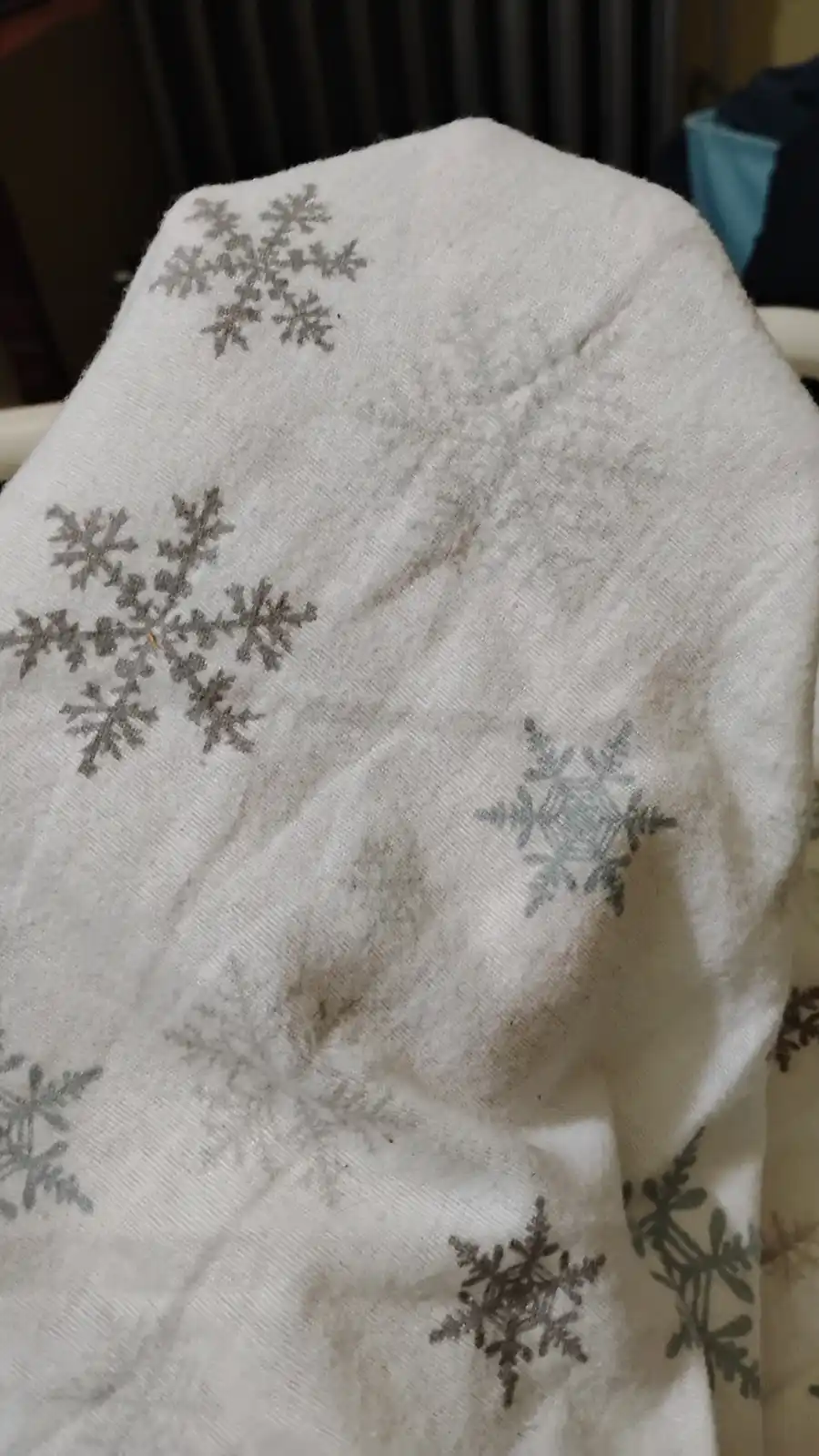 a close-up photo of a white blanket with grey snowflake patterns, visibly stained with dirt and grime, suggesting it's been…
