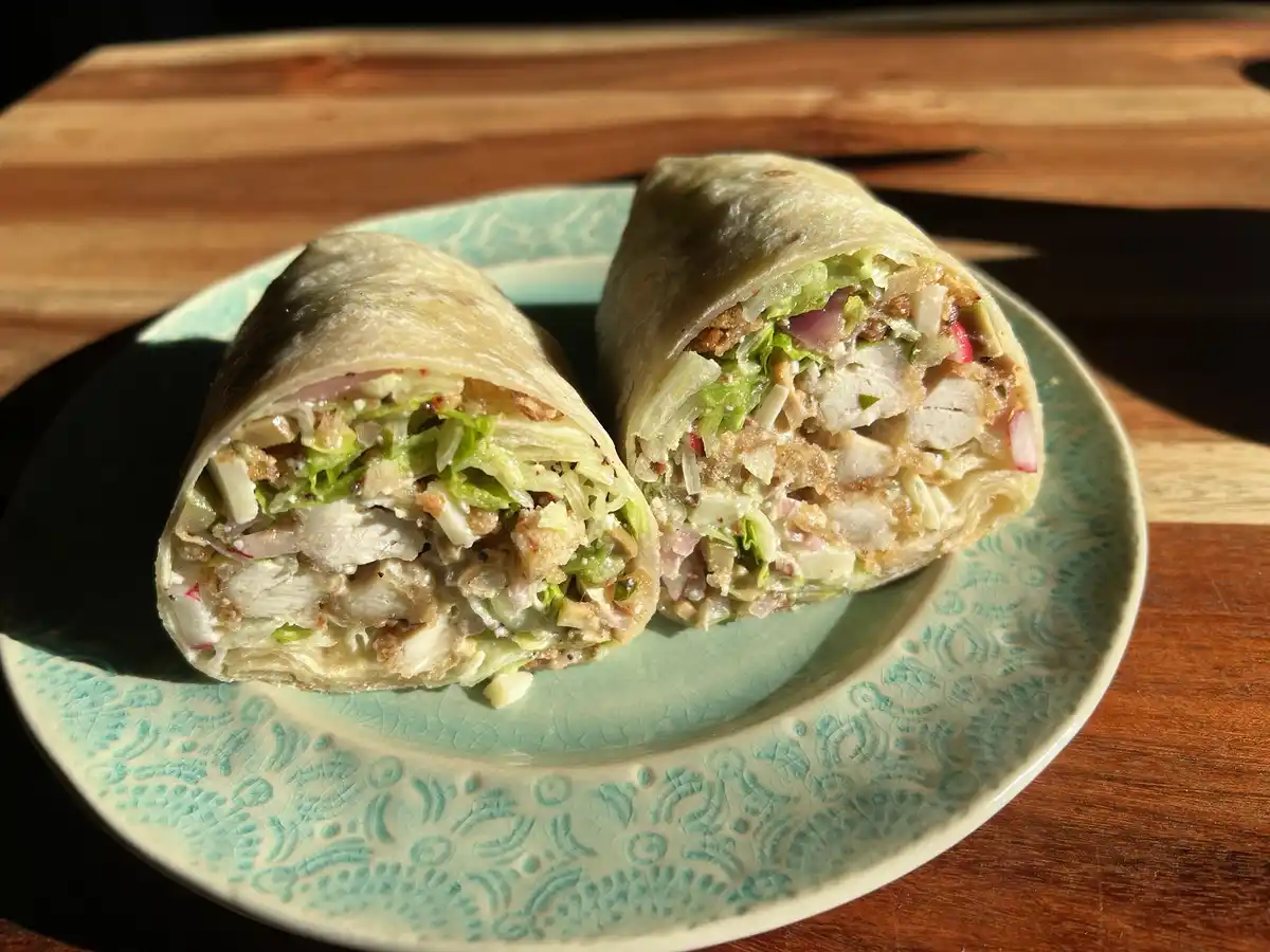 A burrito cut in half and placed on a patterned green plate, revealing fillings of chicken, lettuce, and radishes, with…