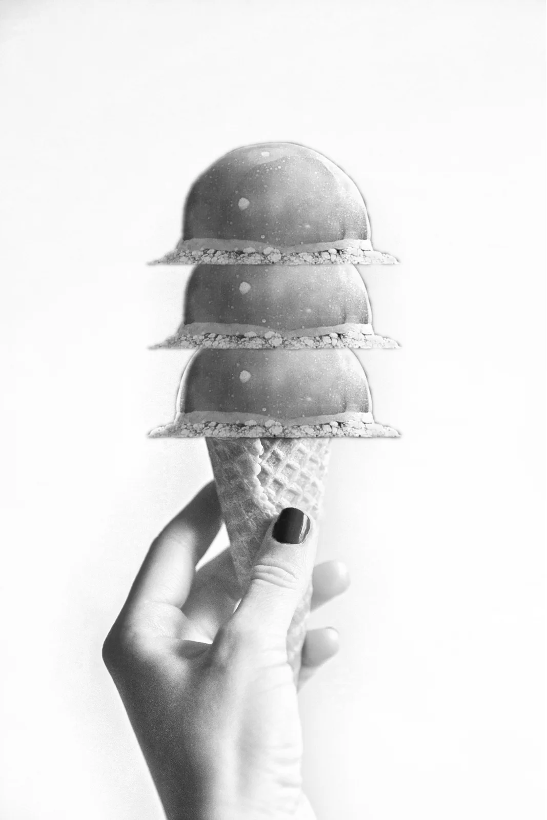 A black and white photo shows a hand holding an ice cream cone with three scoops, each topped with a crumbly crust. The hand…