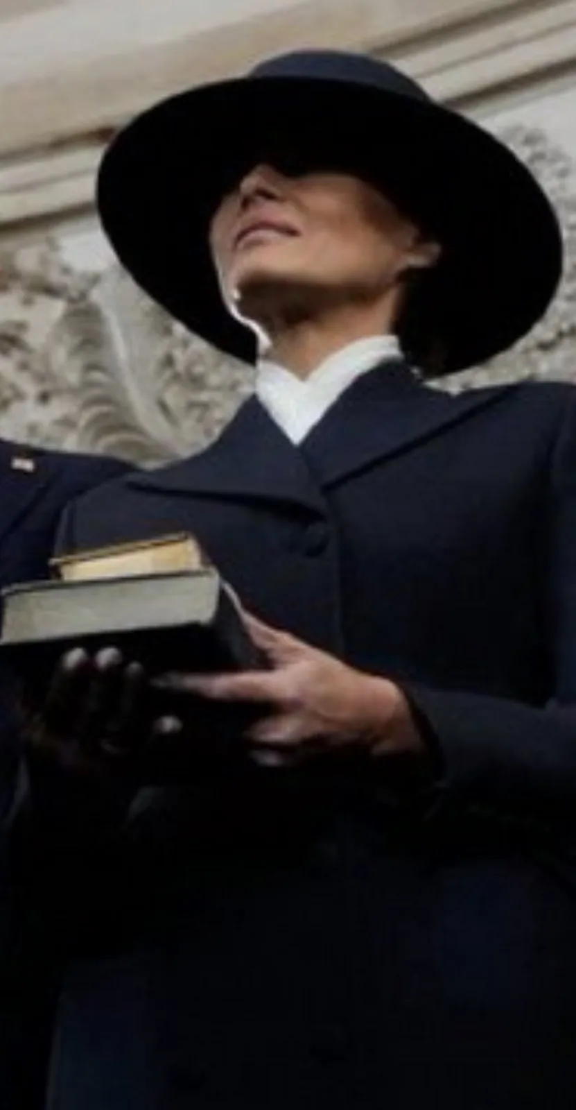 A woman wearing a dark coat and wide-brimmed hat holds two books, looking upward with a serene expression. The overlaid text…
