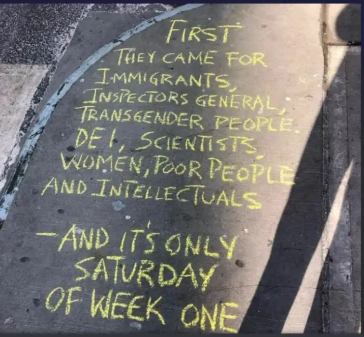 Yellow chalk writing on a dark sidewalk curb lists groups targeted in a satirical 'they came for' progression, ending with…