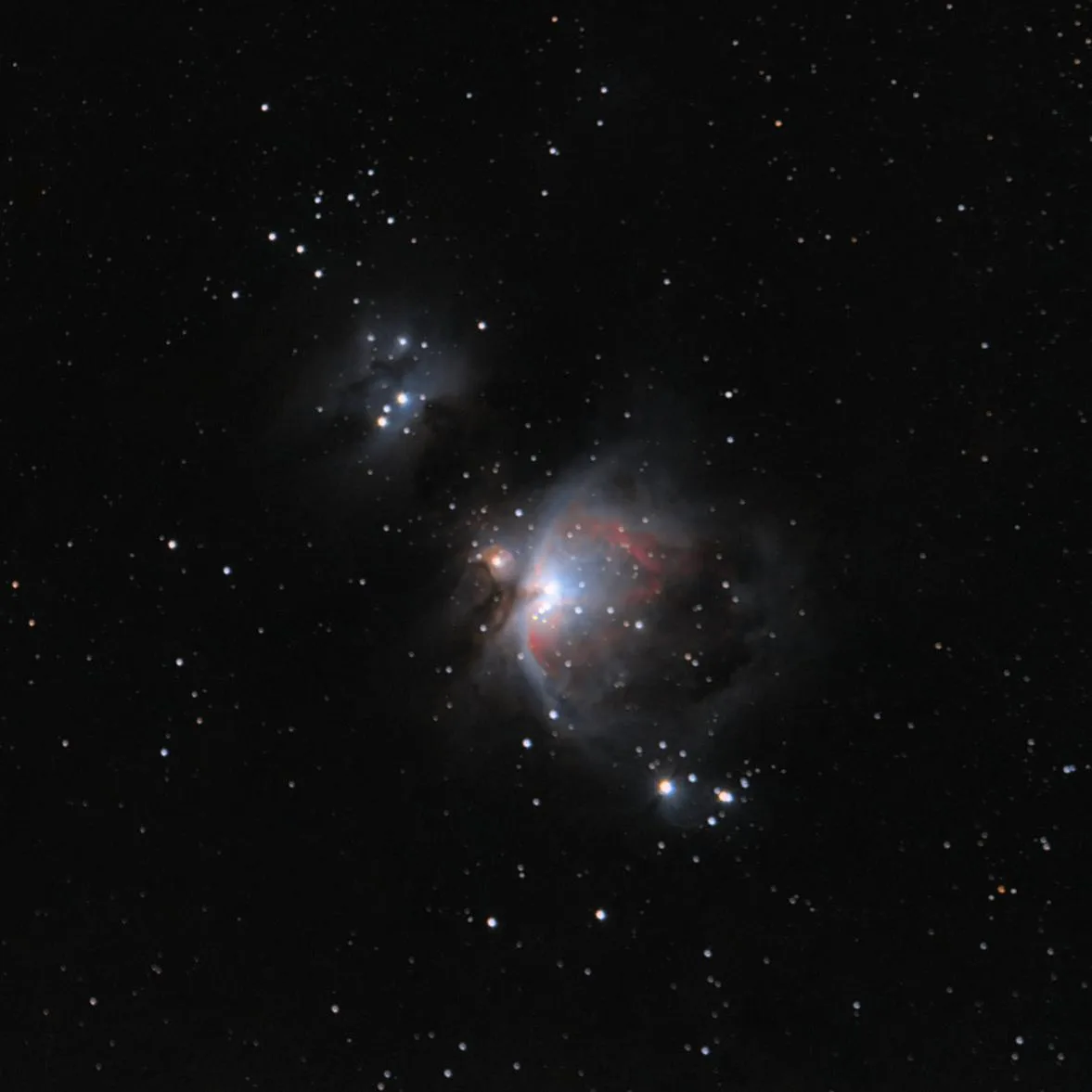 A deep-sky astrophotograph of the Orion Nebula, showing a bright central star surrounded by glowing red and blue gas clouds…