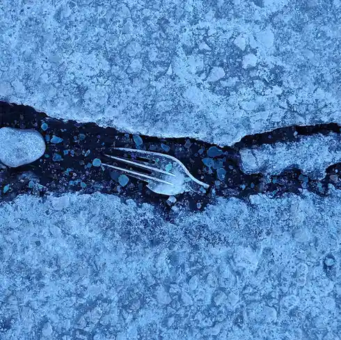 A metal fork lies partially embedded in a narrow crack of frozen ground, surrounded by ice crystals and small stones under a…