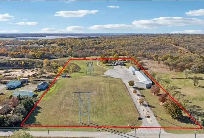 an aerial photo of a rural property with a red outline highlighting the land for sale, which includes several barns, a paved…