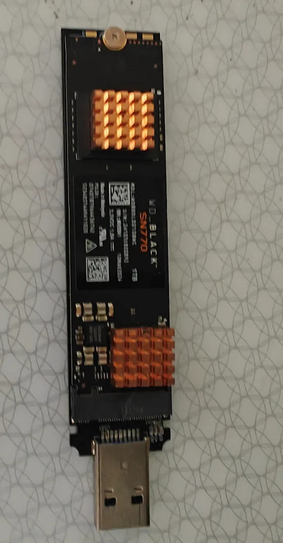 A WD_BLACK SN770 NVMe SSD with a USB-C connector is shown lying on a patterned surface, its two orange LED indicator lights…