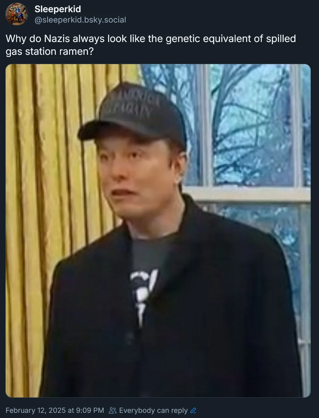 A man wearing a black baseball cap and black coat over a grey t-shirt with a white graphic stands in front of yellow…