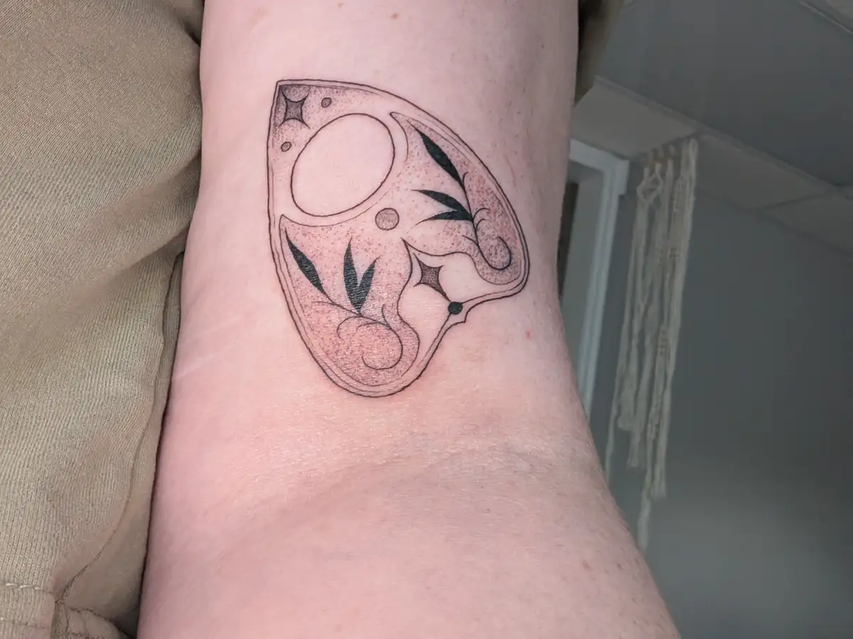 A close-up photo shows a freshly inked black-and-gray tattoo on a person's inner forearm, depicting a stylized slice of…