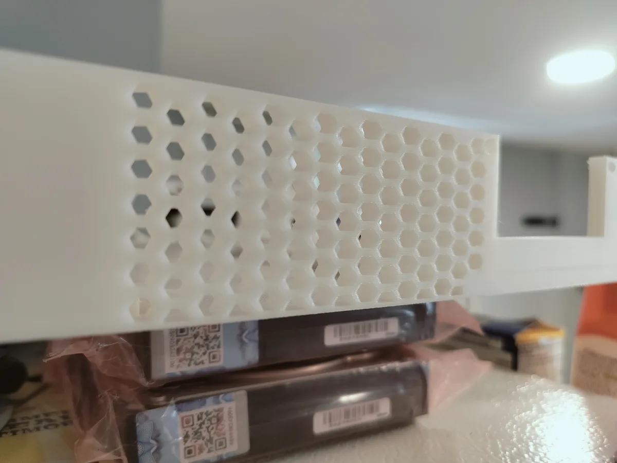 A close-up photo shows a white plastic shelf with a hexagonal honeycomb pattern, resembling a beehive. Below it, packaged…