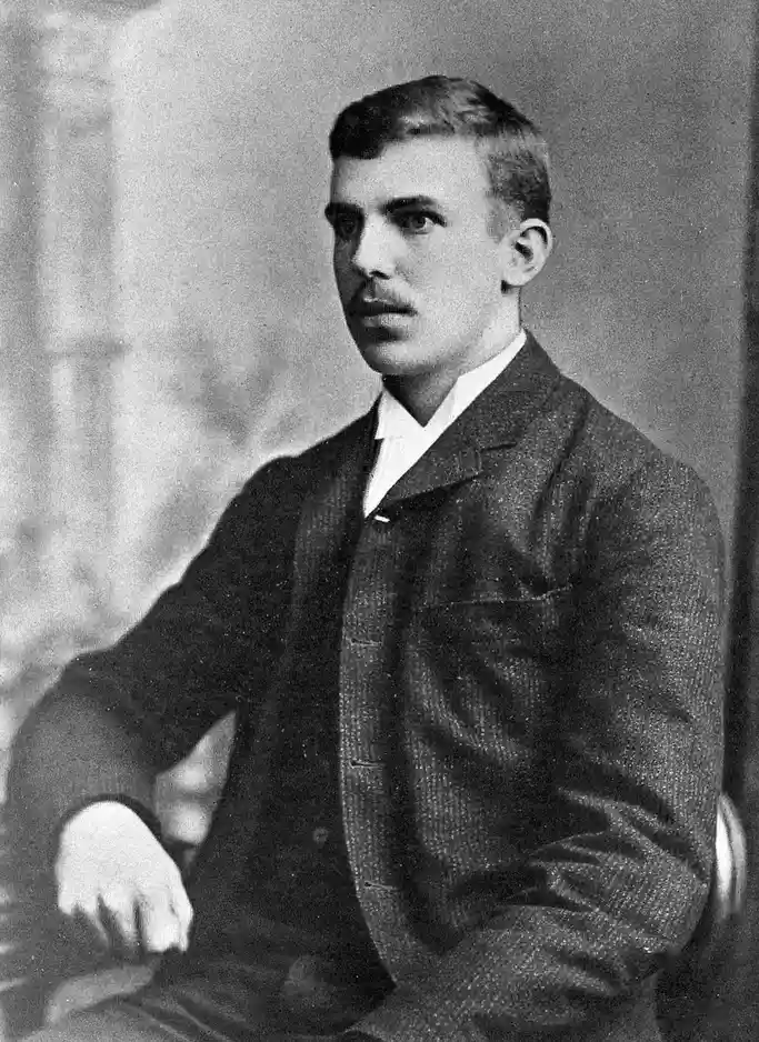 A vintage black-and-white portrait of a young man with a mustache, wearing a textured suit and sitting upright, overlaid…
