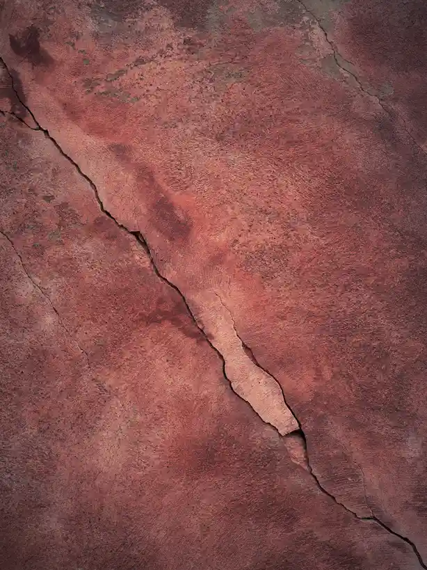 The image shows a close-up of a reddish-brown, textured surface, likely weathered concrete or rock, with a prominent, jagged…