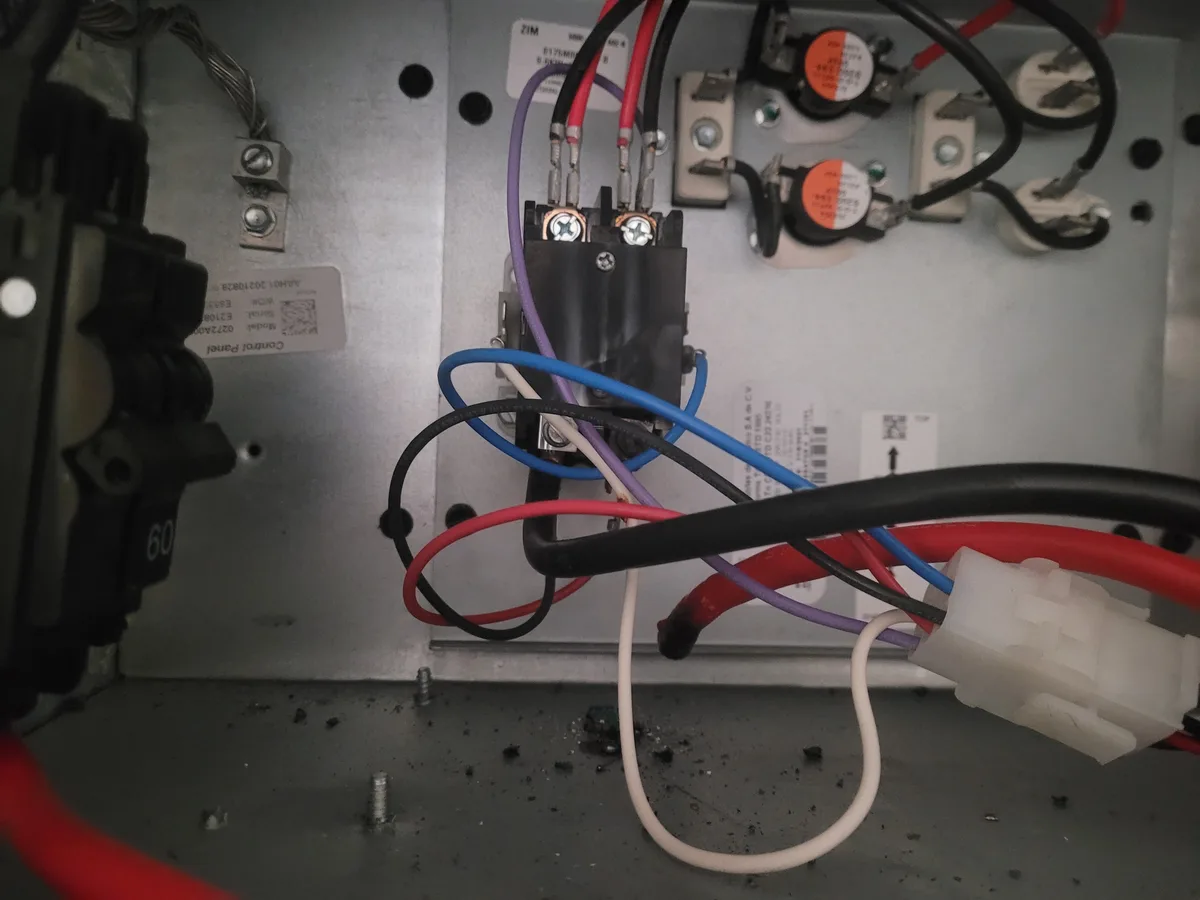 A close-up photo of a messy, tangled electrical control panel with multicolored wires (red, blue, black, purple, white)…