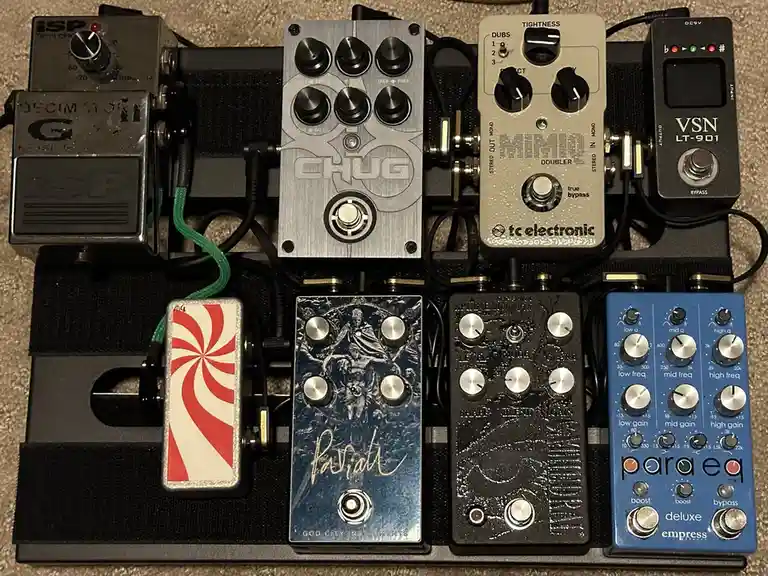 An overhead photo shows a black pedalboard holding eight different guitar effect pedals, each with knobs and footswitches…